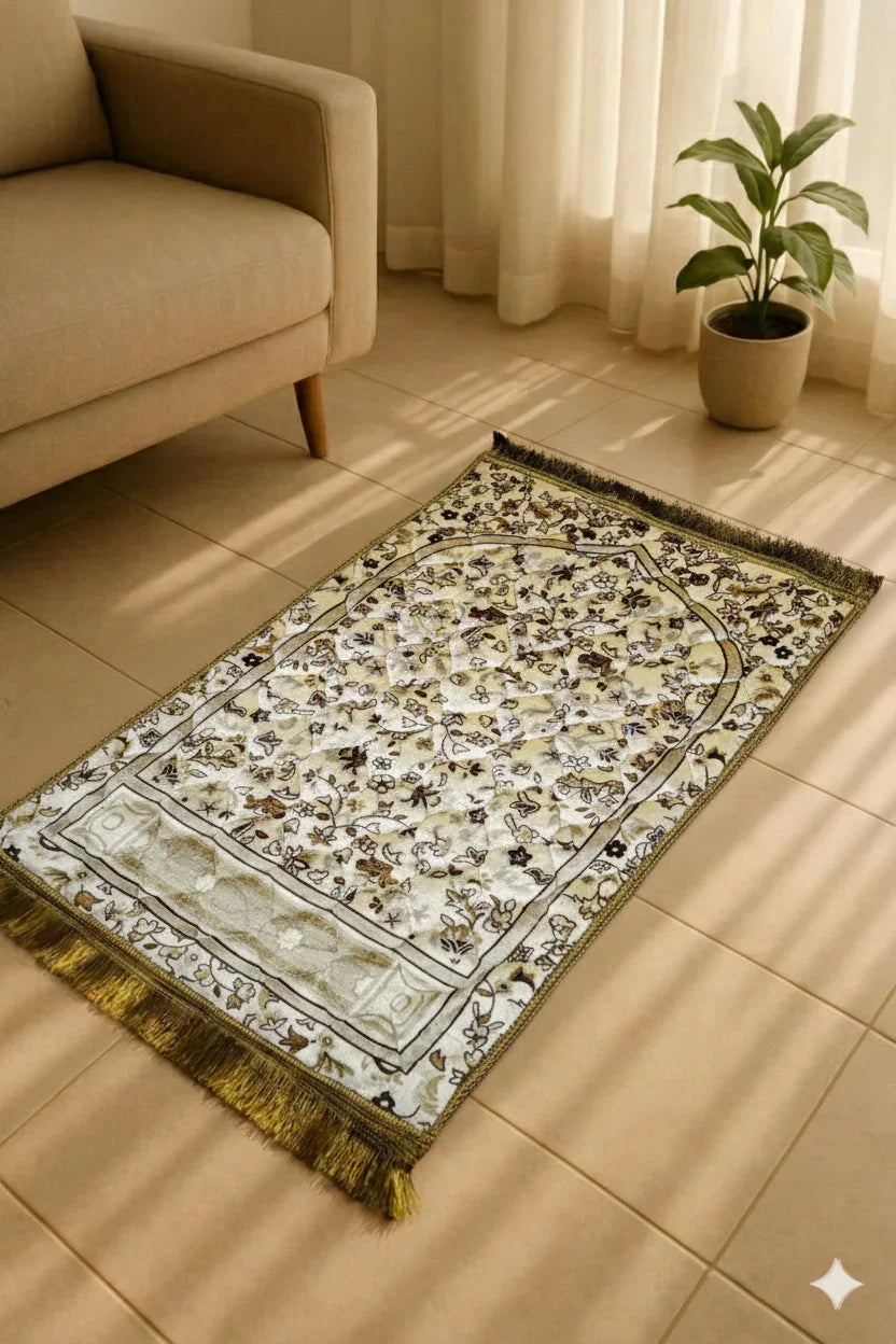 Elegant beige Islamic prayer mat with intricate floral design on tiled floor near beige sofa and potted plant