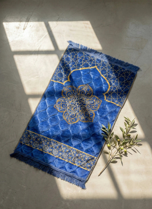 Blue soft velvet prayer mat with intricate gold patterns on a gray floor.