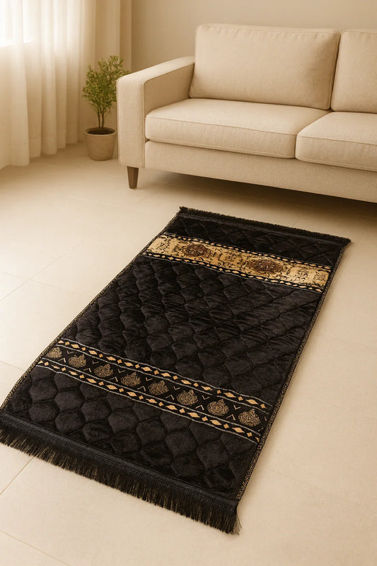 Black Islamic prayer mat with gold geometric patterns on beige floor next to cream sofa and potted plant
