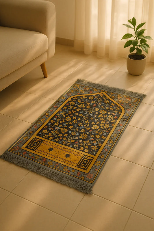 Floral grey Islamic prayer mat with golden border placed on tiled floor near beige sofa and potted plant