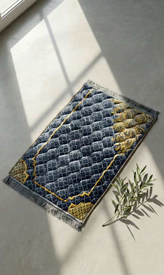 Islamic jay namaz blue and yellow patterned on a light gray floor with a plant.