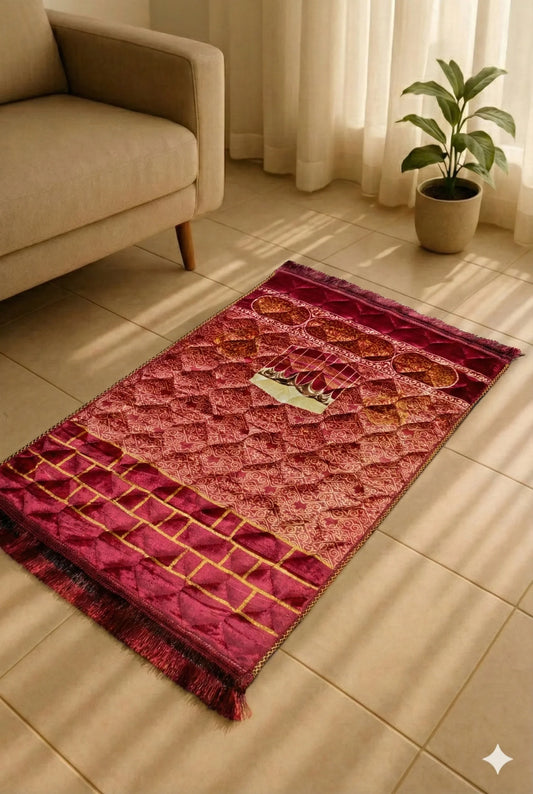 Maroon Islamic prayer mat with geometric and mosque patterns placed beside beige sofa and potted plant