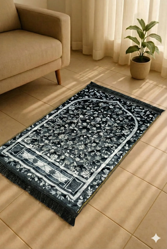 Black and white floral patterned Islamic prayer mat on beige tiled floor near beige sofa and potted plant